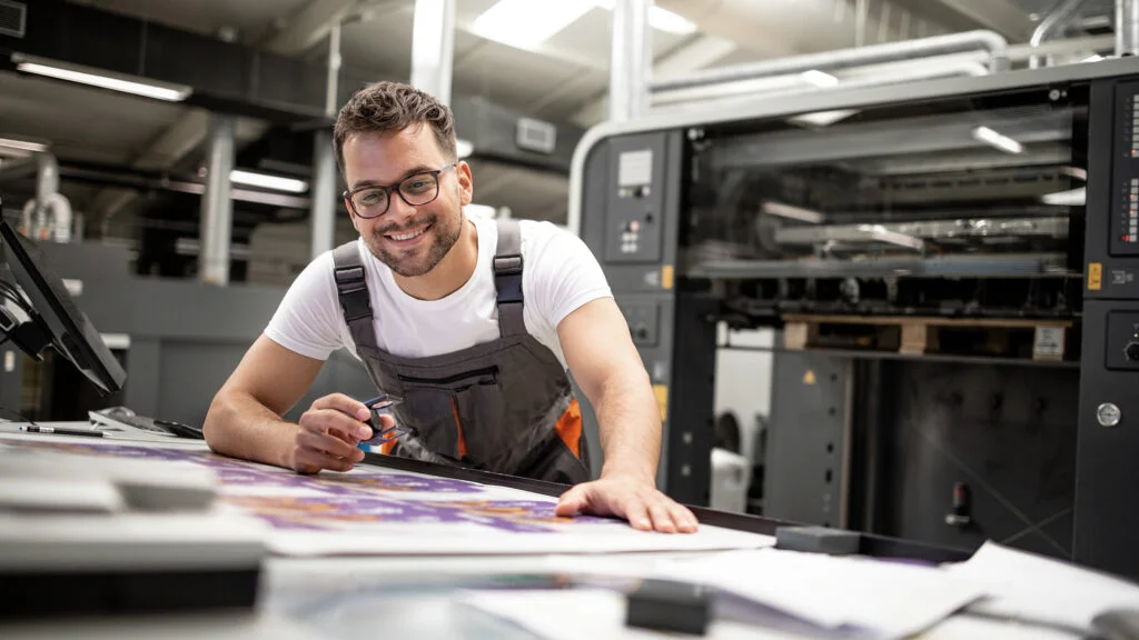 Freundlicher Drucktechniker überprüft die Druckqualität eines Posters in der Druckerei
